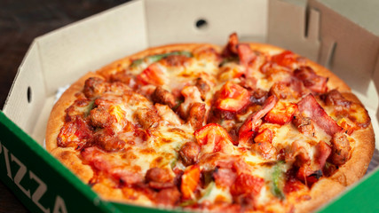 Delicious Italian pizza sliced with bacon, cheese, tomato, capsicum on wooden plate.