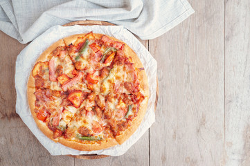 Delicious Italian pizza sliced with bacon, cheese, tomato, capsicum on wooden plate.