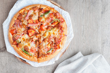 Delicious Italian pizza sliced with bacon, cheese, tomato, capsicum on wooden plate.