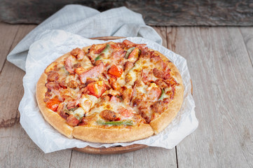 Delicious Italian pizza sliced with bacon, cheese, tomato, capsicum on wooden plate.