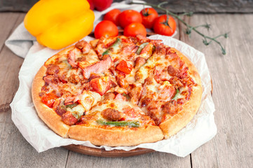 Delicious Italian pizza sliced with bacon, cheese, tomato, capsicum on wooden plate.
