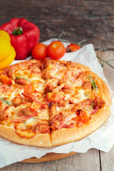 Delicious Italian pizza sliced with bacon, cheese, tomato, capsicum on wooden plate.