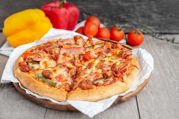 Delicious Italian pizza sliced with bacon, cheese, tomato, capsicum on wooden plate.