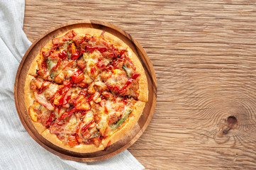 Delicious Italian pizza sliced with bacon, cheese, tomato, capsicum on wooden plate.