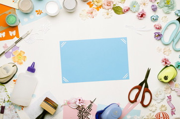 blue card in the center surrounded by colorful paper, scrapbooking materials and paper colors. Top view
