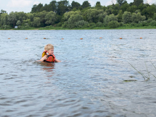 Fototapeta na wymiar Cute little boy in orange life vest swimming in the river
