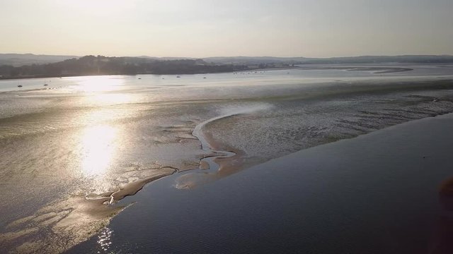 Mass of water view from the sky with the hills and beach in the background. Lympstone is a coastal town and a tourist location with many activities and events. The sun is reflecting in the water.