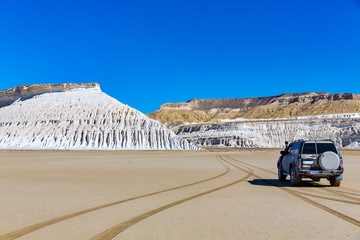 The wonderful views of the steep white cliffs and Tuzbair salt dry lake seen from the SUV driving...