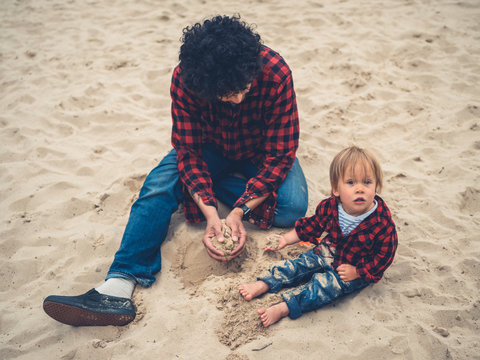 Father and son in identical clothes sitting in sandpit
