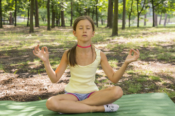 girl's happy and Meditate on the practice of yoga in the park , yoga kid. Healthy lifestyle - little girl doing yoga in the park. Healthy and Yoga Concept