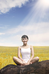 Asian woman enjoying outdoors sitting on the rock at meadow against blue sky