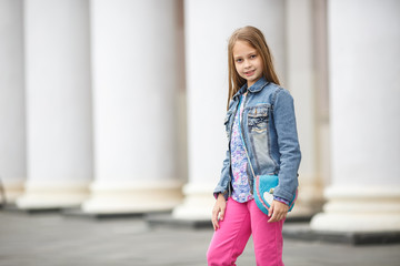 portrait of little beautiful stylish kid girl  on city street near columns