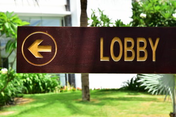 LOBBY. The inscription on a wooden dark board. The arrow indicates the direction. Pointer on the background of palm trees