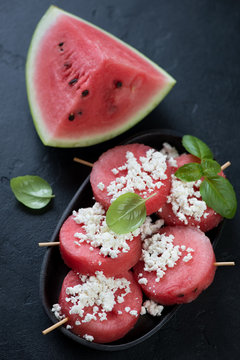 Round watermelon slices on wooden skewers with cottage cheese, black stone background, studio shot