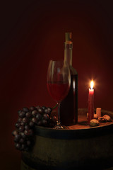 Butelka czerwonego wina w świetle świecy na beczce z winogronem. - obrazy, fototapety, plakaty