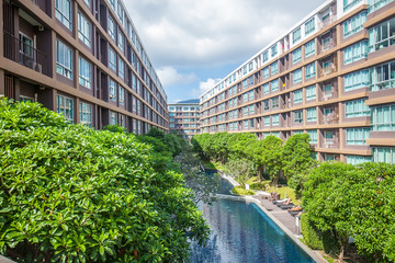Swimming pool with green trees among high rise modern condominium building with pool on Phuket,...