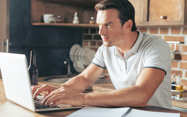 Remote job. Serious nice smart man sitting at the laptop and typing while working at home