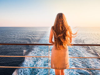 Stylish, beautiful woman on an empty deck of a cruise ship against a background of sea waves, blue sky and sunset - obrazy, fototapety, plakaty