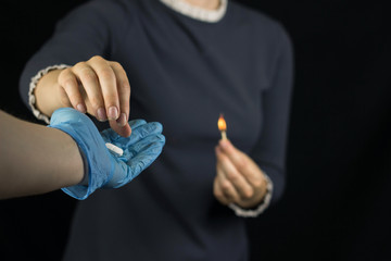 A girl on a black background holds a burning match, pain and burning sensation in the stomach, a man's hand in a glove holds out to her a pill