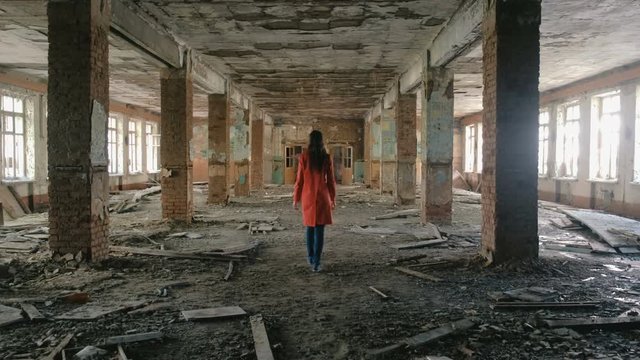 Unrecognizable woman in a red cloak inspects destroyed building after the disaster earthquake, flood, fire.