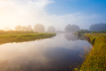 Naklejka na ściany i meble Sunny morning over foggy countryside and river in bright sunlight