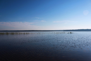 Lake Vysokinskoye in the summer, with the reflection of white clouds in the water. Leningrad Region, Russia.