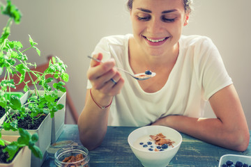 Young beautiful girl woman eating yogurt with flakes and berries for breakfast, healthy food,...