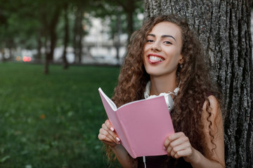 girl student holding book and sitting under tree