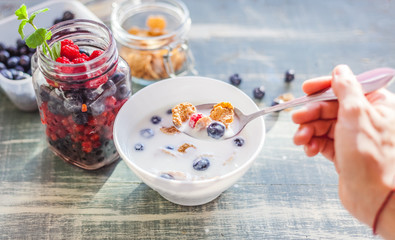 A woman is eating yogurt with cereal and berries for breakfast, holding a spoon, close-up hands, a...