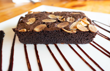 closeup Chocolate brownie with almond on White plate on wooden table .