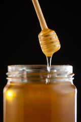 Organic honey drips from wooden dipper in jar