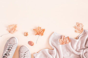 Women fashion clothes on pastel beige background. Sweater, sneakers, dried autumn leaves. Autumn, fall concept. Flat lay, top view