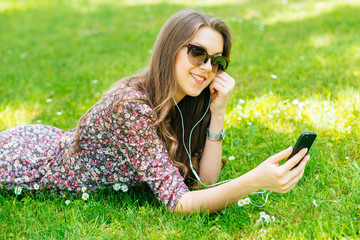 Happy girl or student with smartphone relaxing outdoors in the park