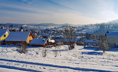 Magnificent winter landscape of the village with roofs of houses pritopornyshennyh snow against the background of mountain slopes on the horizon and blue overcast sky.