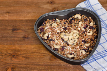 Granola with cashews in a baking sheet. Black wooden table