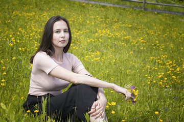 Thoughtful young woman sits on a flower meadow. Summer sunny day