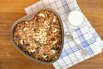 Granola on a baking sheet and yogurt on a wooden table.