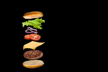 Delicious burger with flying ingredients isolated on black background.