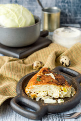 A slice of homemade pie with cabbage on a round wooden plate on an old table. 