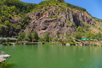 Recreation center with deep green lake on a background of rocky mountain and blue sky