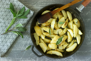 Young fried potatoes with onions and sage in a frying pan on a concrete table.