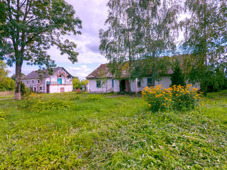 Obraz premium Old buildings in the countryside with a slate roof overgrown with moss with a yard with green grass and a bush of yellow beautiful flowers.