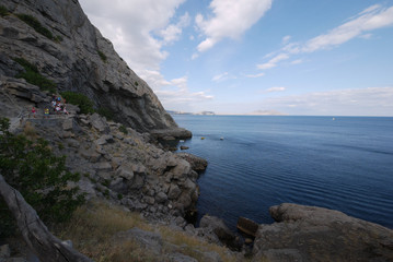 Tourists climbing the stone steps of a steep rocky mountain in the background of the blue boundless sea