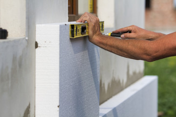 Worker hand with level and knife measuring and cutting white rigid polyurethane foam sheet on wall...