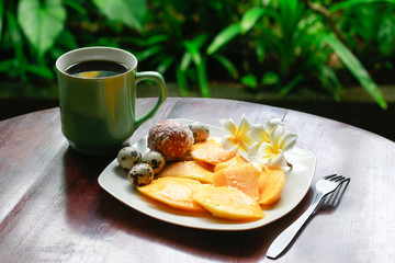 coffee  and plate with mango and eggs on the background of bright greens