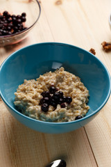 Porridge in a bowl with the berries, walnuts on bright wooden table. Healthy breakfast image. Copy space