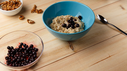 Porridge in a bowl with the berries, walnuts on bright wooden table. Healthy breakfast image. Copy space