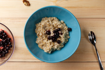 Porridge in a bowl with the berries, walnuts on bright wooden table. Healthy breakfast image. Top view with space