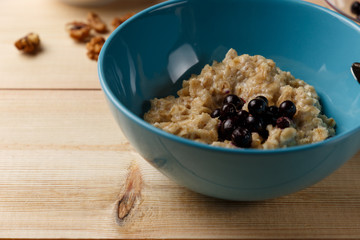 Porridge in a bowl with the berries, walnuts on bright wooden table. Healthy breakfast image. Copy space