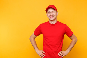 Delivery man in red uniform isolated on yellow orange background. Professional smiling male employee in cap, t-shirt working as courier or dealer standing with arms akimbo. Service concept. Copy space